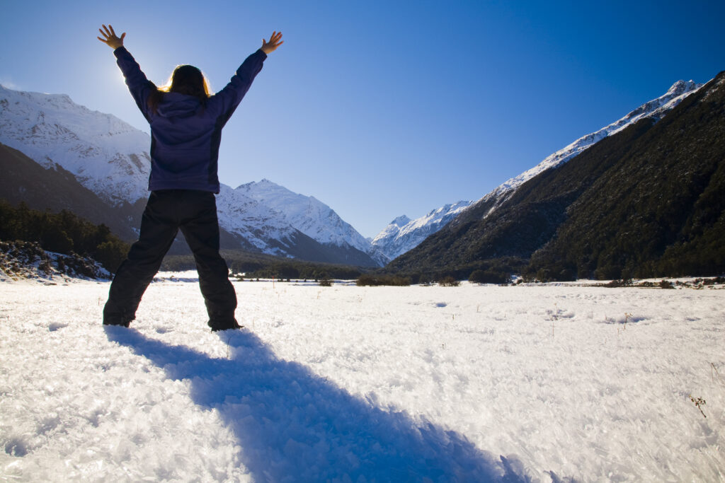 New Zealand, Otago, Mt Aspiring National Park. Tourist in the West Matukituki Valley with arms spead open facing Mt Aspiring.