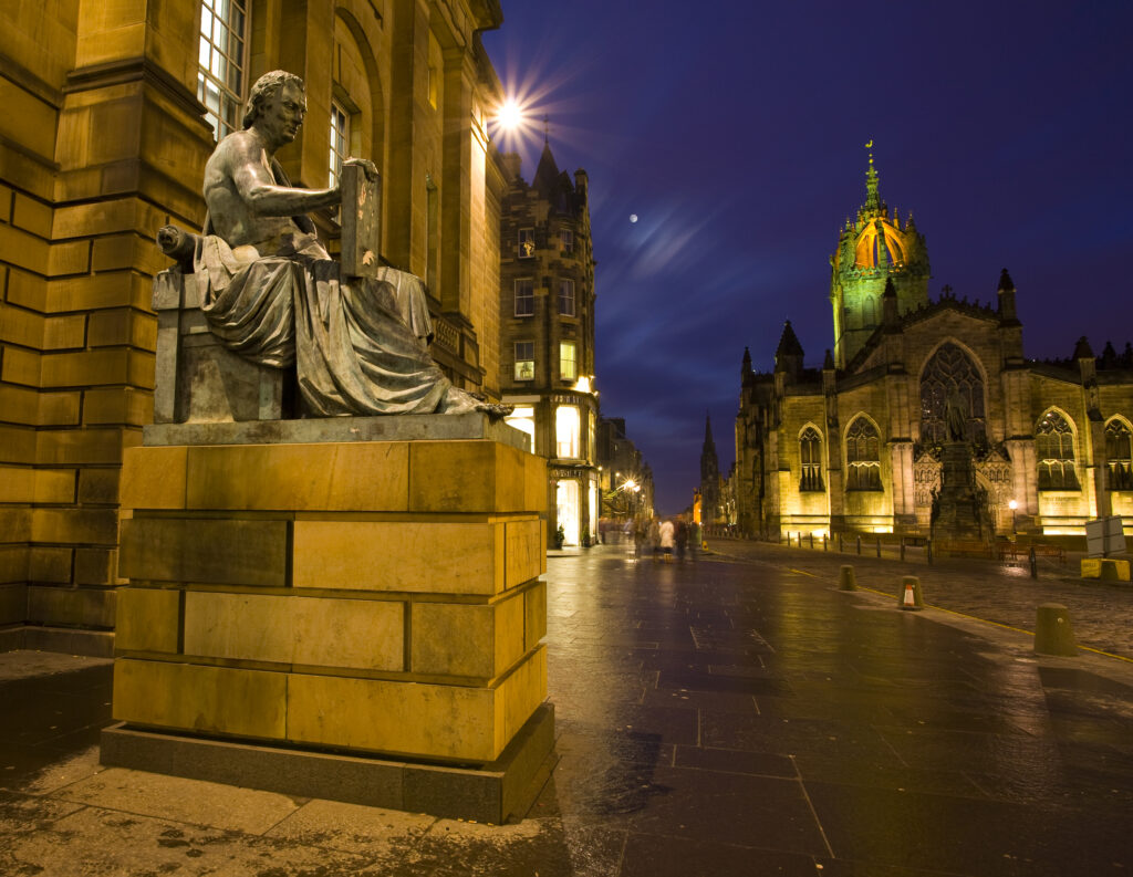 Scotland, Edinburgh, The Royal Mile. Hume statue with the St Giles Cathedral, situated along the Royal Mile.