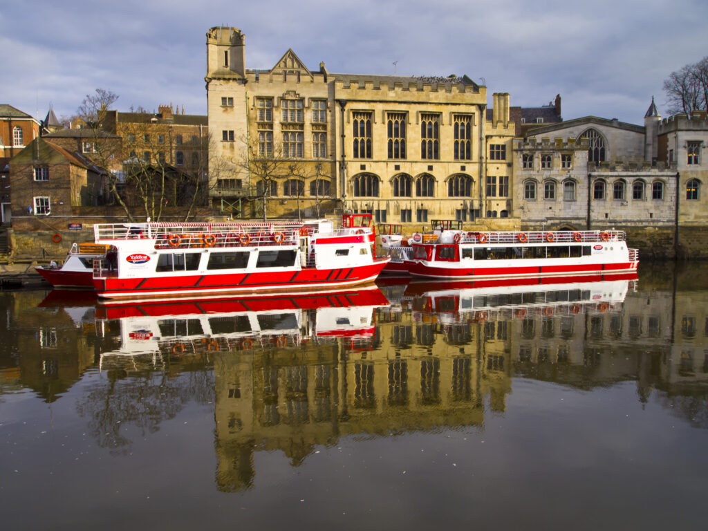 England, North Yorkshire, York City. York city river cruise boats moored on the River Ouse with the Guildhall in the Background.