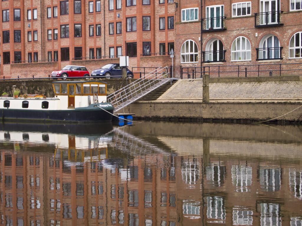 England, North Yorkshire, York City. Modern housing developement and moored canal narrow boat, reflected in the still waters of the River Ouse.