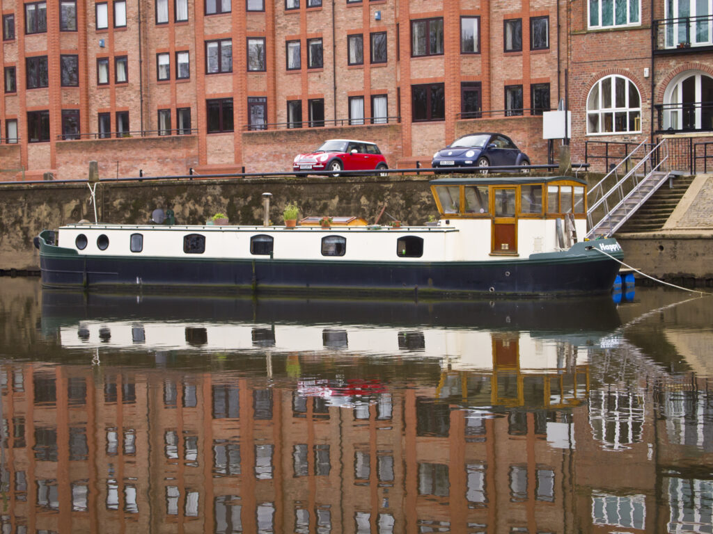England, North Yorkshire, York City. Modern housing developement and moored canal narrow boat, reflected in the still waters of the River Ouse.