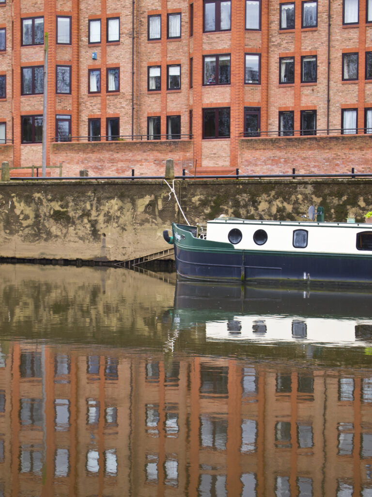 England, North Yorkshire, York City. Modern housing developement and moored canal narrow boat, reflected in the still waters of the River Ouse.
