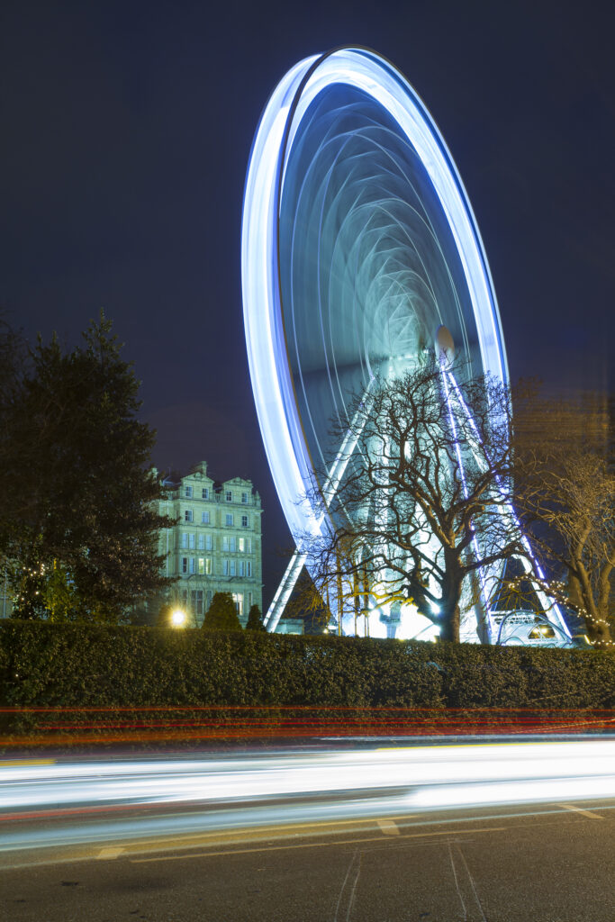 England, North Yorkshire, York City. York Eye Ferris wheel reflected at dusk with passing road traffic.