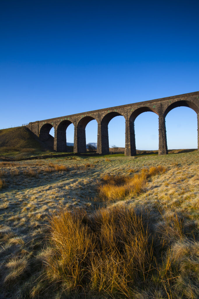 England, North Yorkshire, Yorkshire Dales National Park. Ribblehead Viaduct, a railway viaduct across the valley of the River Ribble at Ribblehead in the Yorkshire Dales, with the peak of Whernside in the distance viewed on a frosty, spring morning.