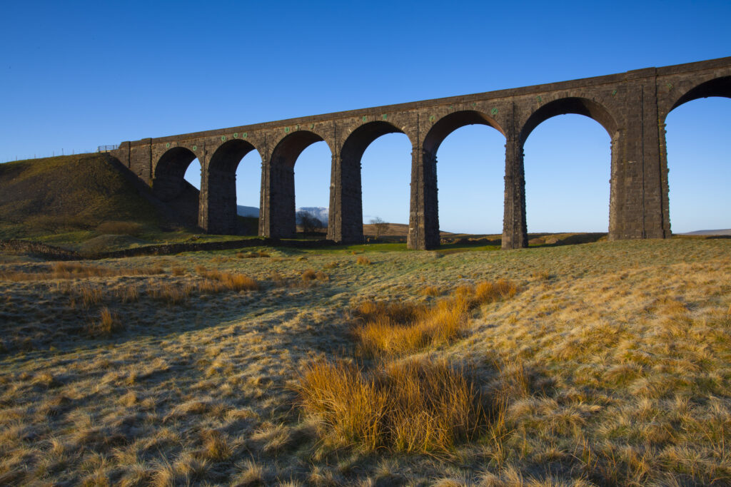 England, North Yorkshire, Yorkshire Dales National Park. Ribblehead Viaduct, a railway viaduct across the valley of the River Ribble at Ribblehead in the Yorkshire Dales, with the peak of Whernside in the distance viewed on a frosty, spring morning.