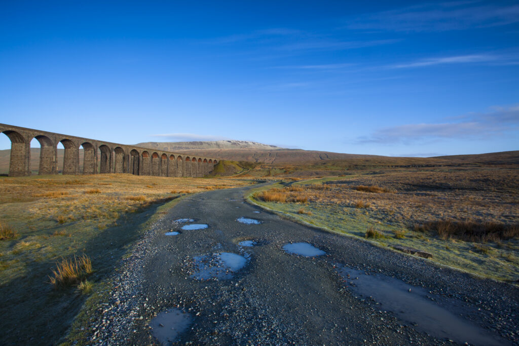 England, North Yorkshire, Yorkshire Dales National Park. Ribblehead Viaduct, a railway viaduct across the valley of the River Ribble at Ribblehead in the Yorkshire Dales, with the peak of Whernside in the distance viewed on a frosty, spring morning.