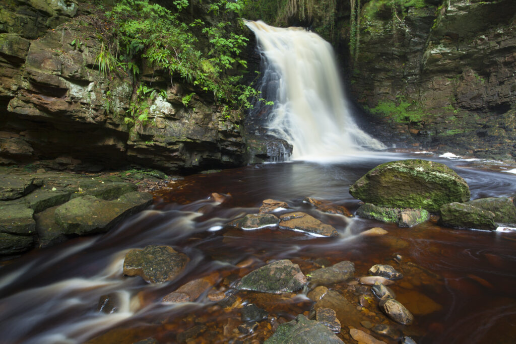 England, Northumberland, Hareshaw Linn. Hareshaw Linn is a spectacular waterfall located in a steep sided gorge, which continues to flow through a wooded valley. Hareshaw Linn is located near Bellingham within the Northumberland National Park.