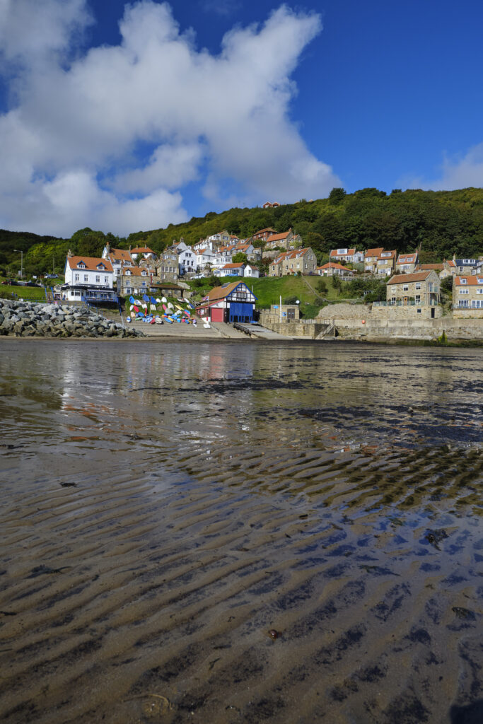 England, North Yorkshire, Runswick Bay. Small coastal village reflected in the wet, low tide, sand of Runswick Bay.