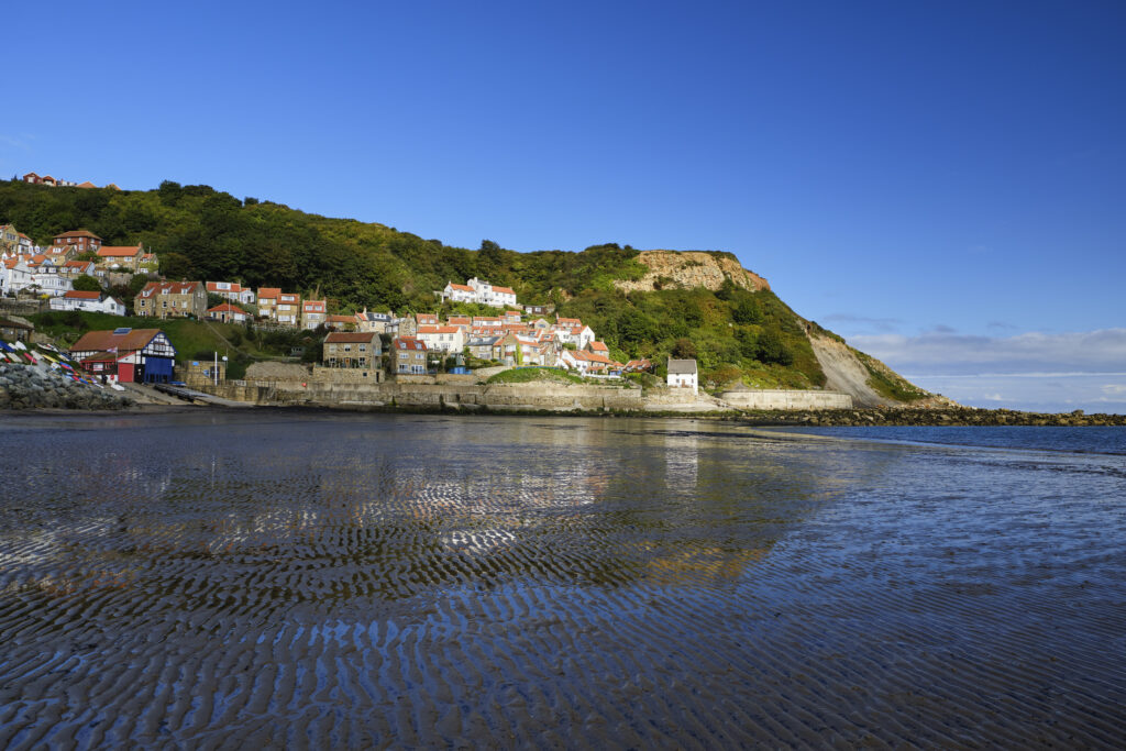 England, North Yorkshire, Runswick Bay. Small coastal village reflected in the wet, low tide, sand of Runswick Bay.