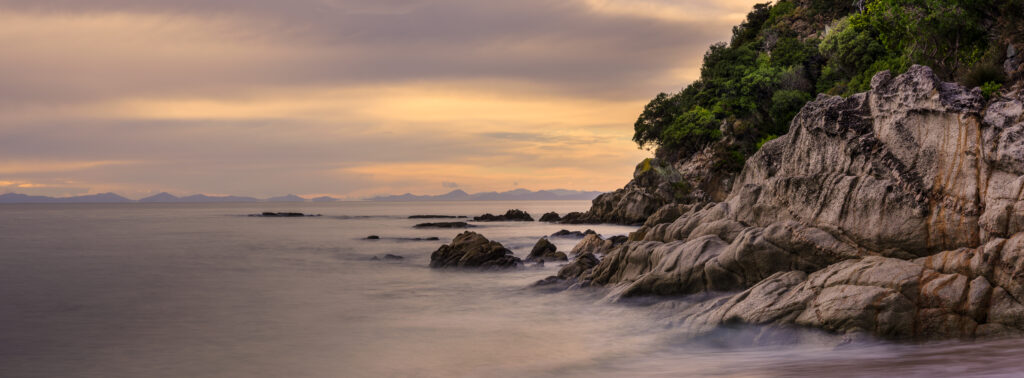 New Zealand, Nelson & Marlborough, Abel Tasman National Park. Dawn at the golden sand beach of Totaranui Bay which is bordered by native woodland and rocky outcrops.