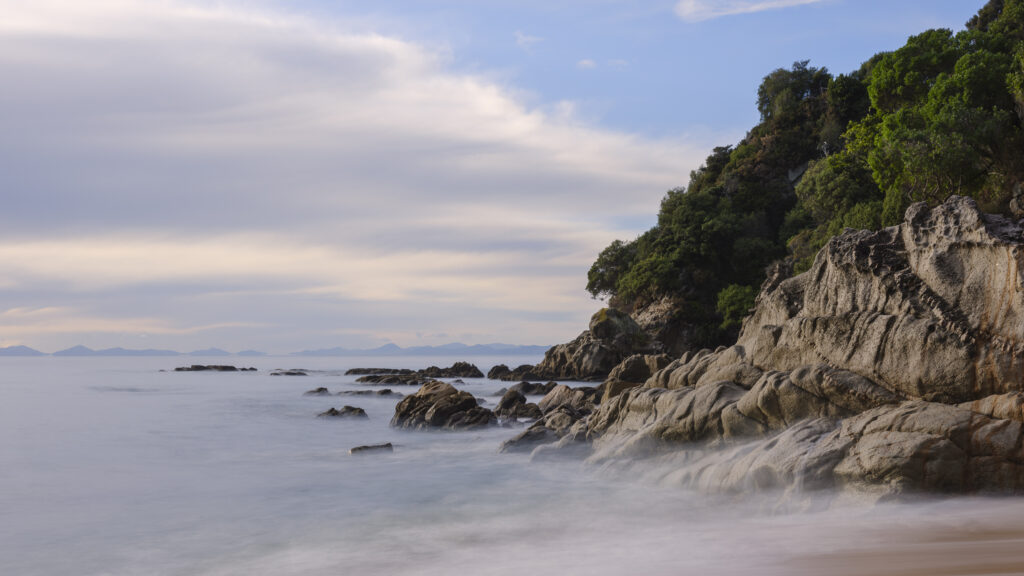 New Zealand, Nelson & Marlborough, Abel Tasman National Park. Dawn at the golden sand beach of Totaranui Bay which is bordered by native woodland and rocky outcrops.