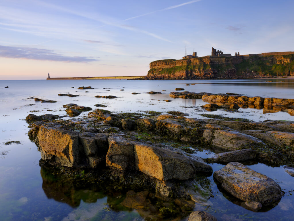 England, Tyne and Wear, Tynemouth. Soft morning light just after dawn at King Edward's Bay in Tynemouth with Tymouth Priory in the distance.