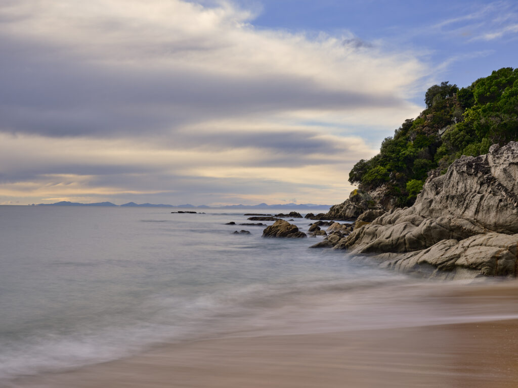 New Zealand, Nelson & Marlborough, Abel Tasman National Park. Dawn at the golden sand beach of Totaranui Bay which is bordered by native woodland and rocky outcrops.