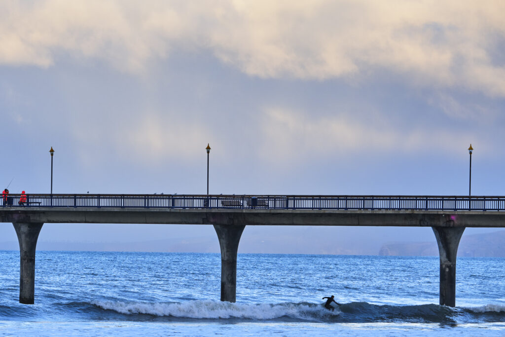 New Zealand, Christchurch, New South Brighton. Surfer below the pier at New South Brighton beach.