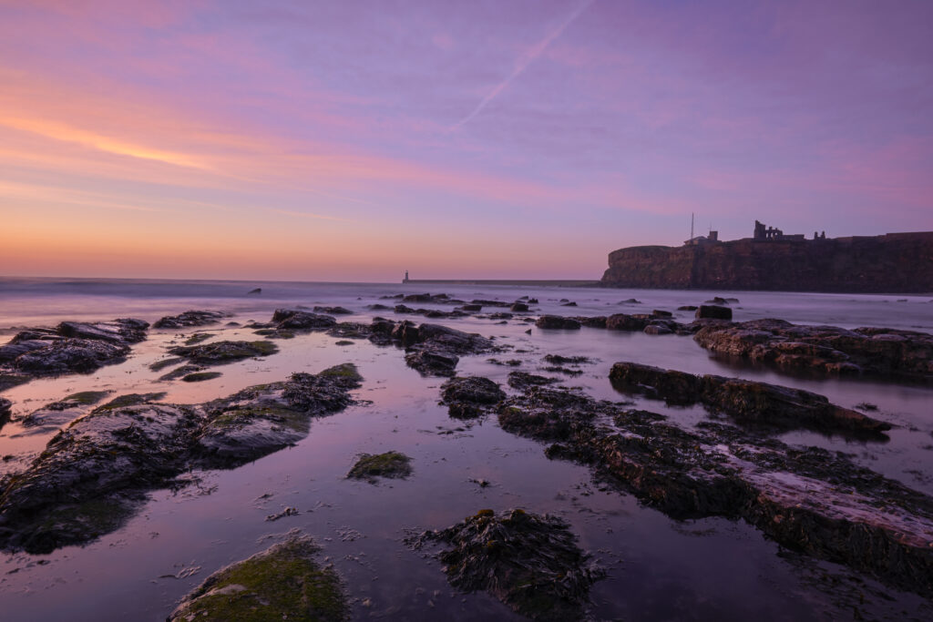 England, Tyne and Wear, Tynemouth. Dawn at King Edward's Bay in Tynemouth with Tymouth Priory in the distance.