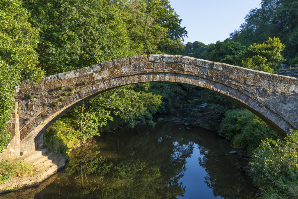 England, North Yorkshire, North York Moors National Park. Beggar's Bridge, a tradtional arched bridgfe designed to carry walkers and horses over the River Esk in Glaisdale.