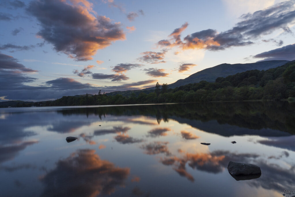 England, Cumbria, Lake District National Park. Lakeland hills and a colourful sunset reflected upon the still face of Coniston Water.