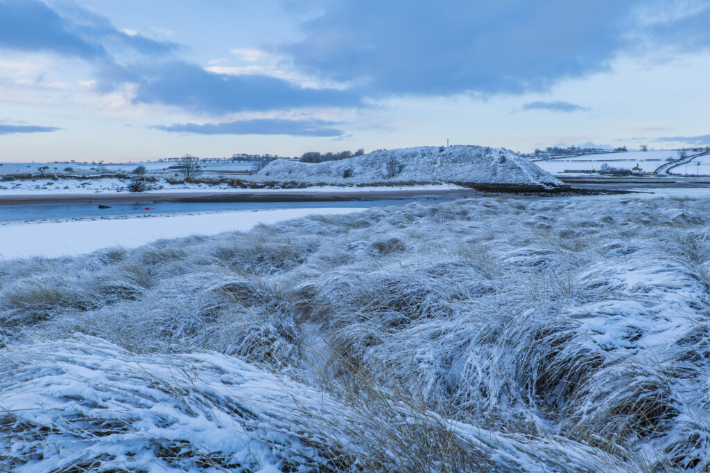 England, Northumberland, Alnmouth. Snow covered sand dunes near the mouth of the Aln Estuary at Alnmouth. The hill in the distance is known as Church Hill.