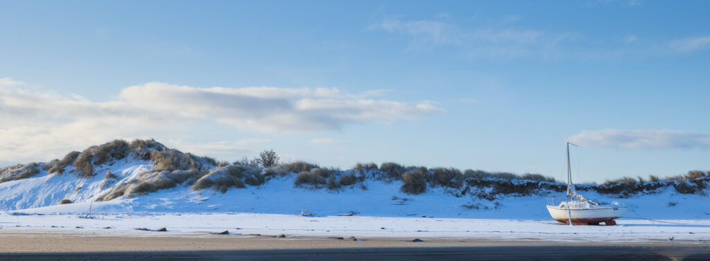 England, Northumberland, Alnmouth. Snow covered sand dunes and boat near the mouth of the Aln Estuary at Alnmouth.