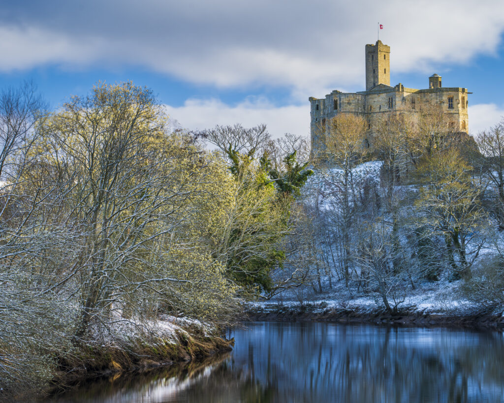 England, Northumberland, Warkworth. Warkworth Castle and surrounding snow covered landscape, reflected upon the still waters of the River Coquet on a winter morning.