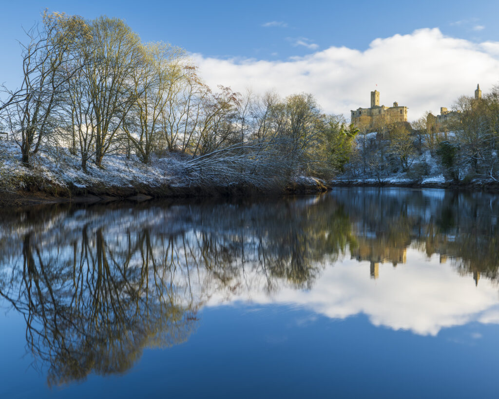 England, Northumberland, Warkworth. Warkworth Castle and surrounding snow covered landscape, reflected upon the still waters of the River Coquet on a winter morning.