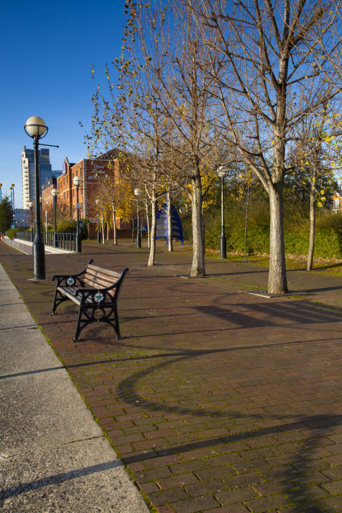 England, Greater Manchester, Salford Quays. Bench on walkway alongside Ontario Basin located on the Salford Quays in the City of Salford in Greater Manchester.