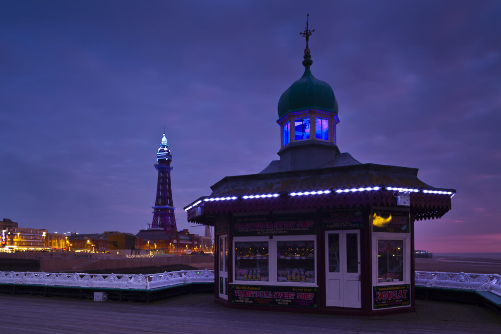England, Lancashire, Blackpool. Traditional English Sweet Shop located on the historic Black Pool North Pier with the Black Pool Tower in the distance.
