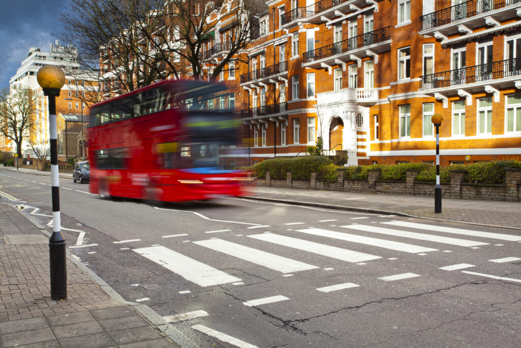 England, London, Abbey Road. A red London bus approaches the famous pedestrian crossing at Abbey Road, made famous by the cover of the Beatles album of the same name.
