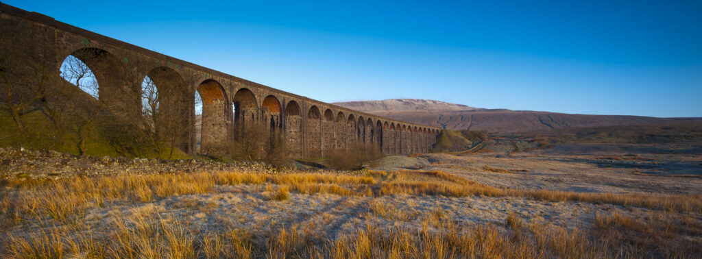 England, North Yorkshire, Yorkshire Dales National Park. Ribblehead Viaduct, a railway viaduct across the valley of the River Ribble at Ribblehead in the Yorkshire Dales, with the peak of Whernside in the distance viewed on a frosty, spring morning.