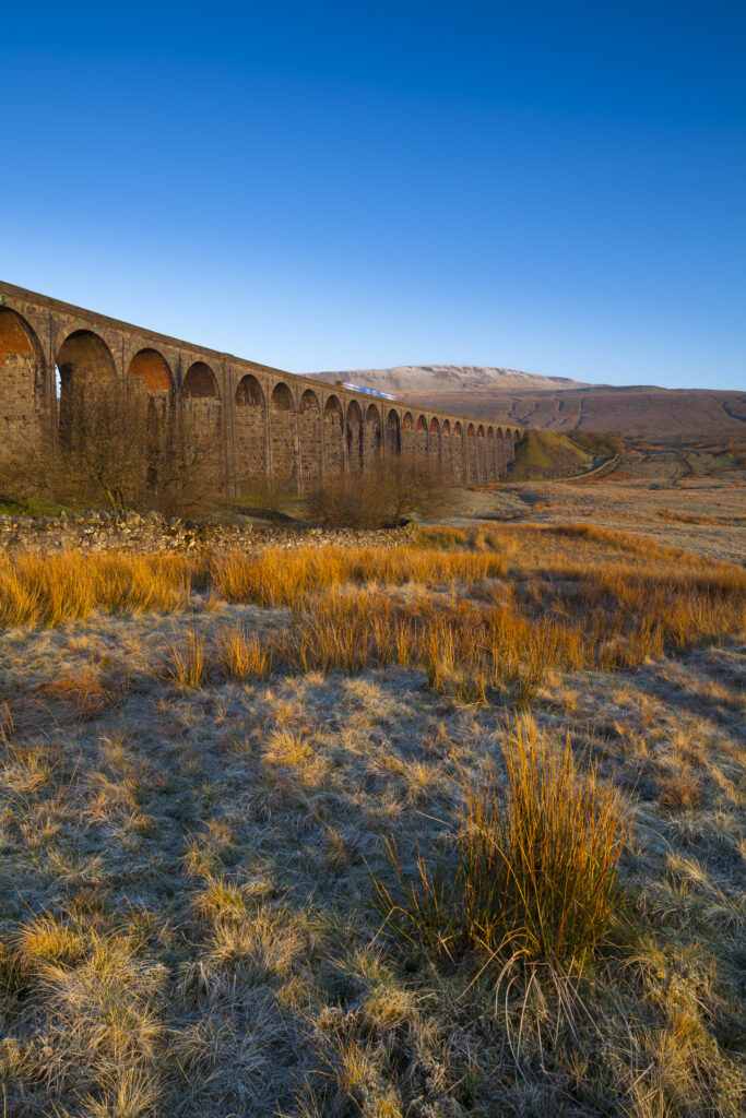 England, North Yorkshire, Yorkshire Dales National Park. Ribblehead Viaduct, a railway viaduct across the valley of the River Ribble at Ribblehead in the Yorkshire Dales, with the peak of Whernside in the distance viewed on a frosty, spring morning.