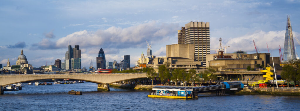 England, Greater London, London South Bank / River Thames. Festival Pier (river boat station), Waterloo Bridge, St Pauls Cathedral, the Gherkin and the financial city of london in the distance.