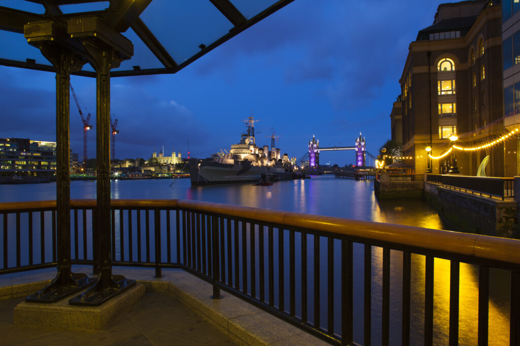 England, London, Southwark. HMS Belfast, originally a Royal Navy light cruiser, permanently moored in London on the River Thames with Tower Bidge and the Tower of London in the distance.