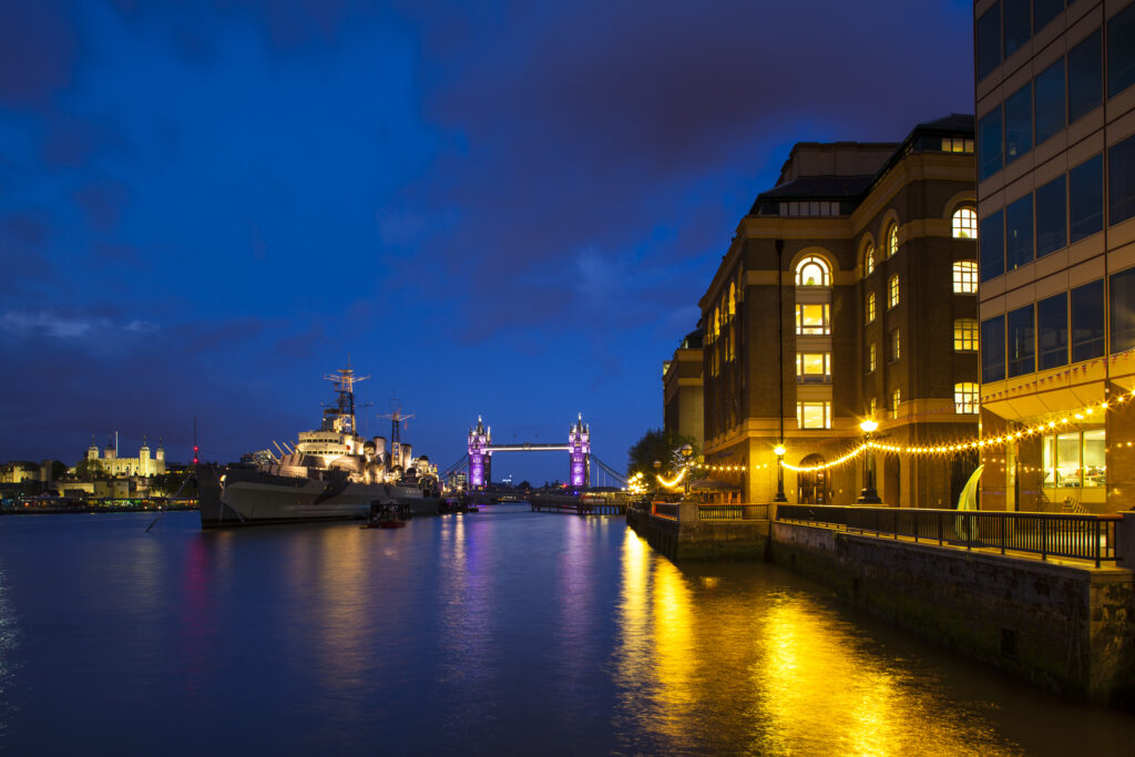 England, London, Southwark. HMS Belfast, originally a Royal Navy light cruiser, permanently moored in London on the River Thames with Tower Bidge and the Tower of London in the distance.