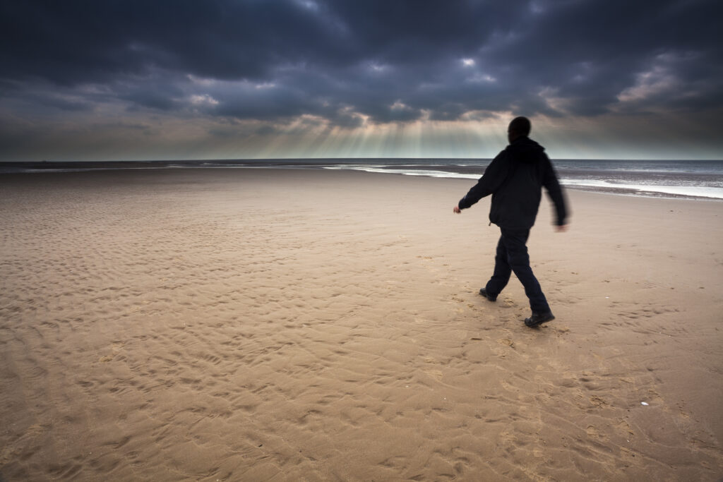 England, Lancashire, Blackpool. Hiker walking along the South Shore beach with distant storm above the Irish Sea.