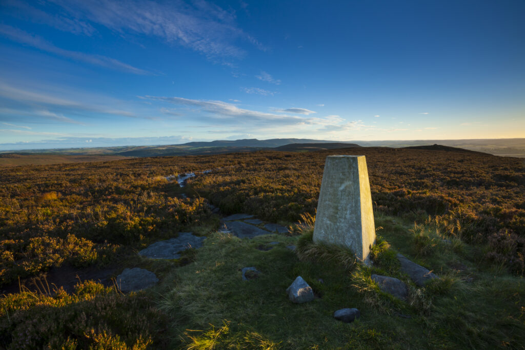 England, Northumberland, Northumberland National Park. Trig point on Long Crag, looking towards the Simonside Hills.