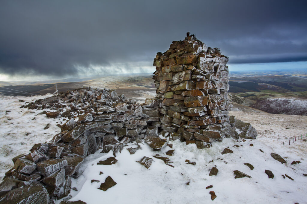 England, Northumberland, Northumberland National Park. A dusting of snow on the cairn at the summit of Auchope Rig, part of the Cheviot, looking towards the Scottish Border Ridge.