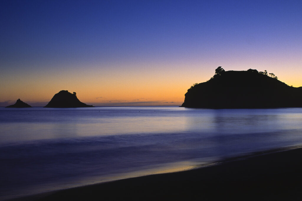 NEW ZEALAND, Coromandel, Hahei Beach. A colourful sunrise behind the off shore islands of the beach