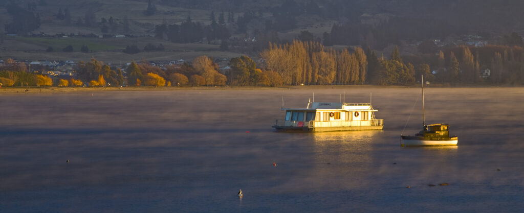 New Zealand, Otago, Lake Wanaka. The warm hues of sunset highlight the rising mist engulfing boats anchored on Lake Wanaka.