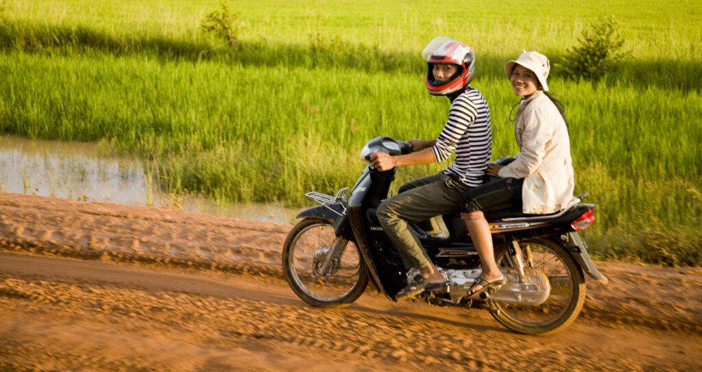 Girls riding along a dirt road in Cambodia.