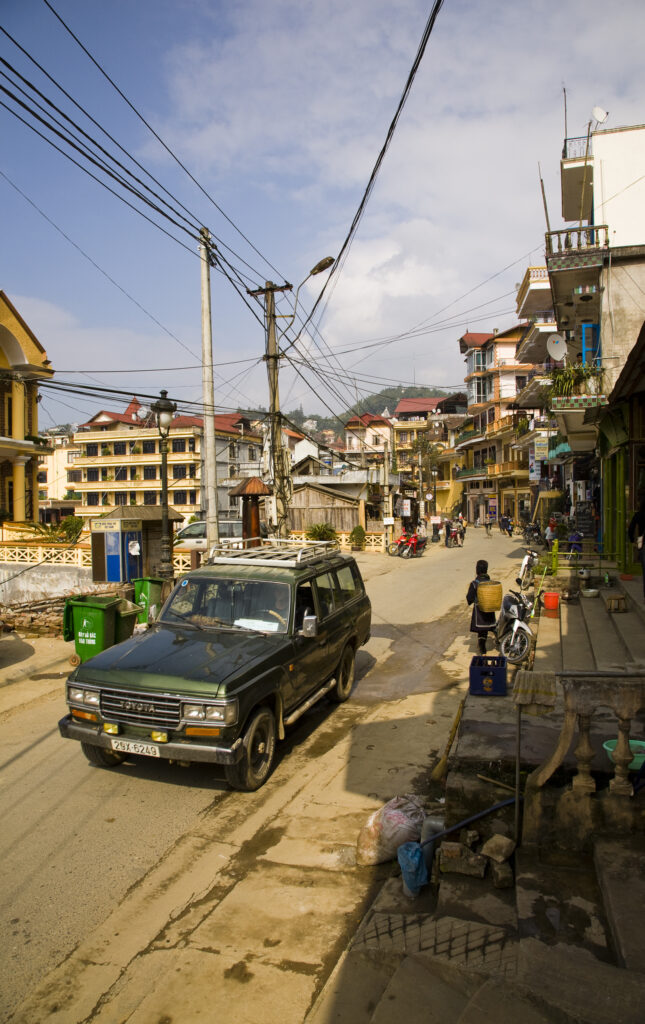 Vietnam, Northern Vietnam, Sapa. 4 wheel drive and hill tribe woman, in a general street scene of Sapa.