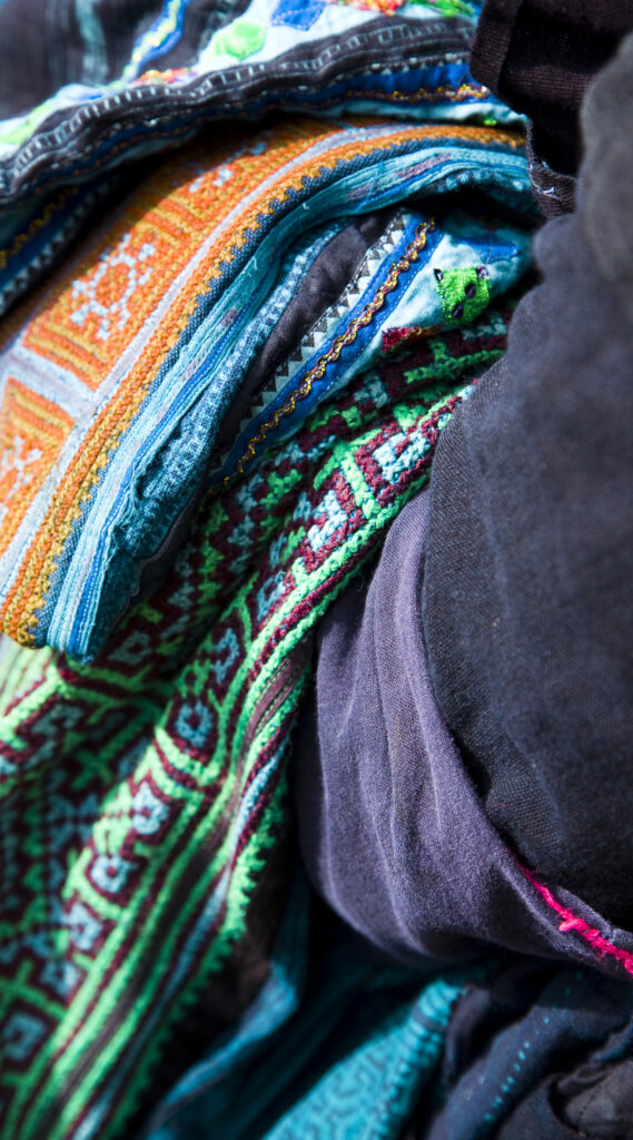 Vietnam, Northern Vietnam, Sapa. Hill tribe clothing and blankets hanging over the arm of a hill tribe woman trying to sell her wares to tourists.