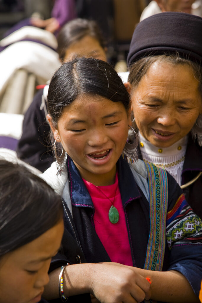 Vietnam, Northern Vietnam, Sapa. Hill tribe girls and an elder woman share a joke at a busy market in Sapa.