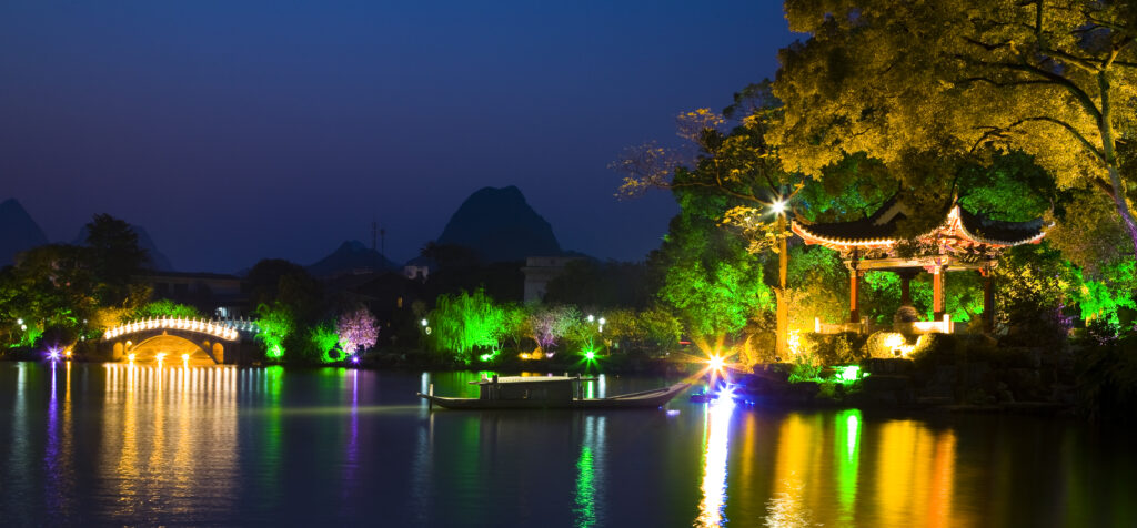 China, Guangxi Zhuang Autonomous Region, Guilin City. Pagoda and lake in downtown Guilin City, surrounded by trees floodlit with numerous colours.