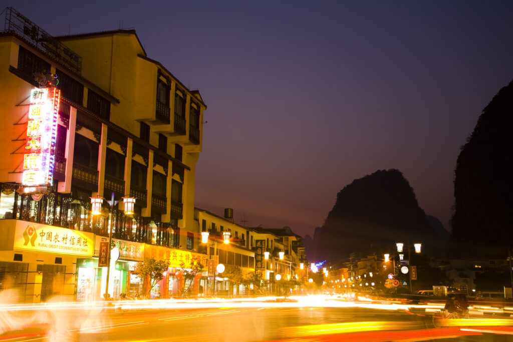 China, Guangxi Zhuang Autonomous Region, Yangshuo City. Busy traffic running through a chinese city at night with a backdop of limestone karst hills.