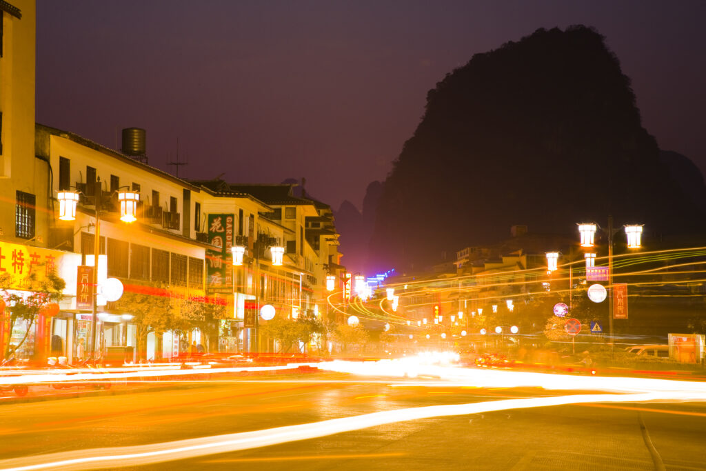 China, Guangxi Zhuang Autonomous Region, Yangshuo City. Busy traffic running through a chinese city at night with a backdop of limestone karst hills.