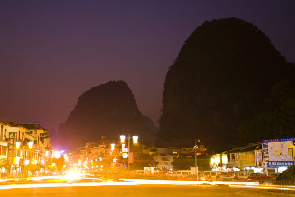 China, Guangxi Zhuang Autonomous Region, Yangshuo City. Busy traffic running through a chinese city at night with a backdop of limestone karst hills.