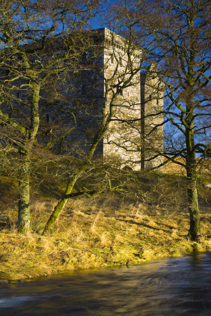 Scotland, Scottish Borders, Hermitage Castle. Hermitage water running in front of the Hermitage Castle. The castle has a somewhat colourful history with numerous stories of war, treason and murder being associated with the property. It was built in an area considered to be a key element in the English and Scottish wars for control over the Liddesdale and the border area.
