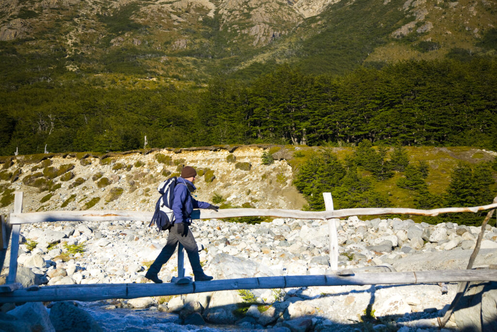 Argentina, Patagonia, Los Glaciares National Park. Hiker using a rustic bridge to cross a river by the Poincenot campsite, below the Fitz Roy range.
