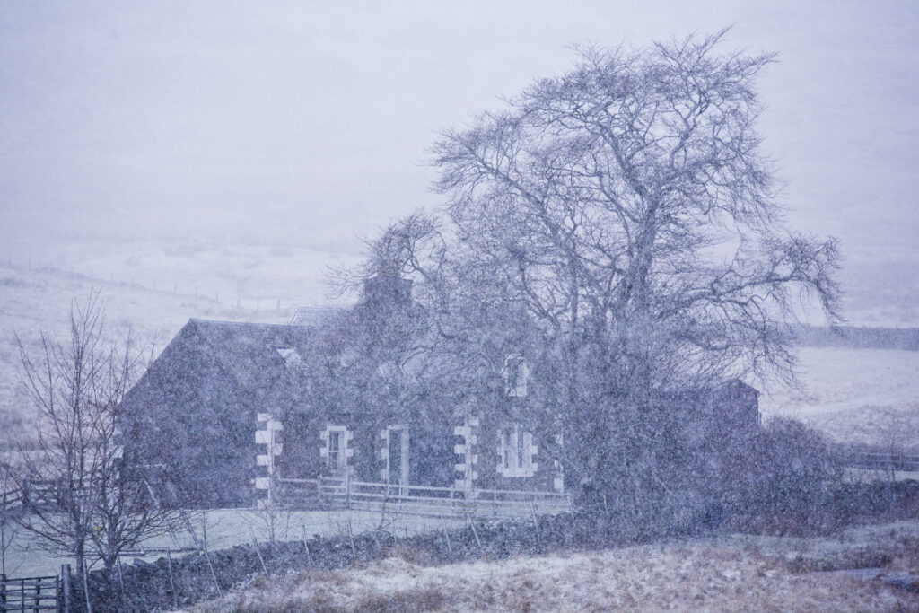 Scotland, Scottish Borders, Glentude Hill. A snow blizzard engulfs a farm house situated near the remote Glenlude Hill.
