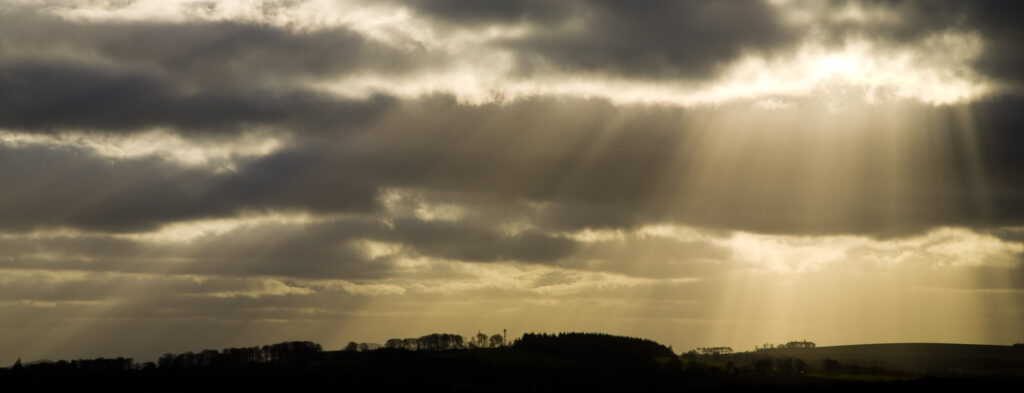 Scotland, Scottish Borders, Harelaw Moor. Shafts of light break through storm clouds near Harelaw Moor.